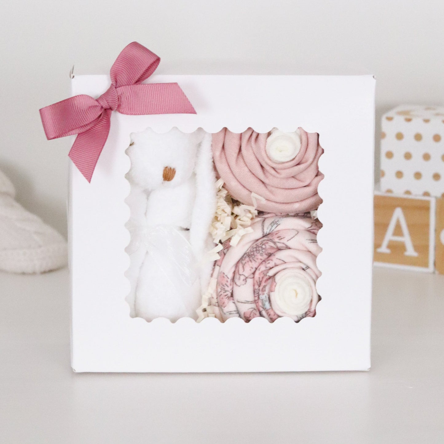 Baby lovey and blanket sock cupcakes with pink and white elements in a box with a pink ribbon on a light background