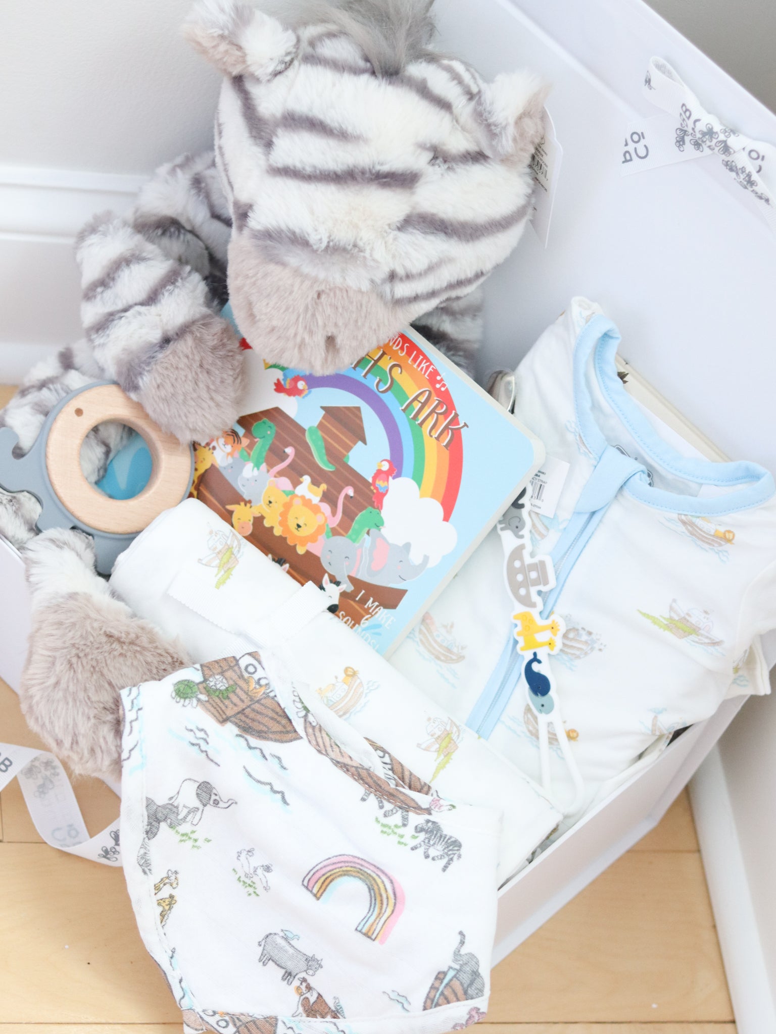 Noah's Ark Baby items including a bib, plush toys, and a book in a box on a wooden surface.