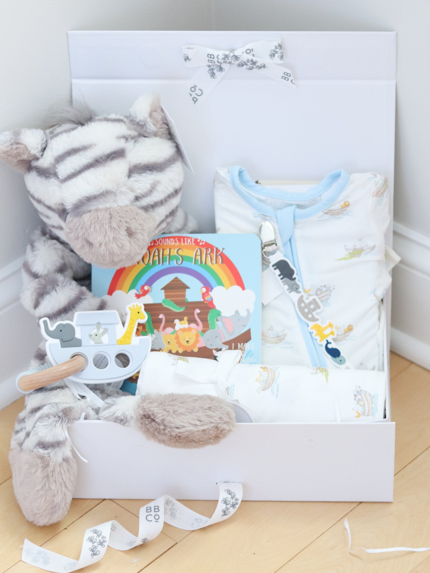 Gift box with plush toy, baby bib, and book on a wooden floor.