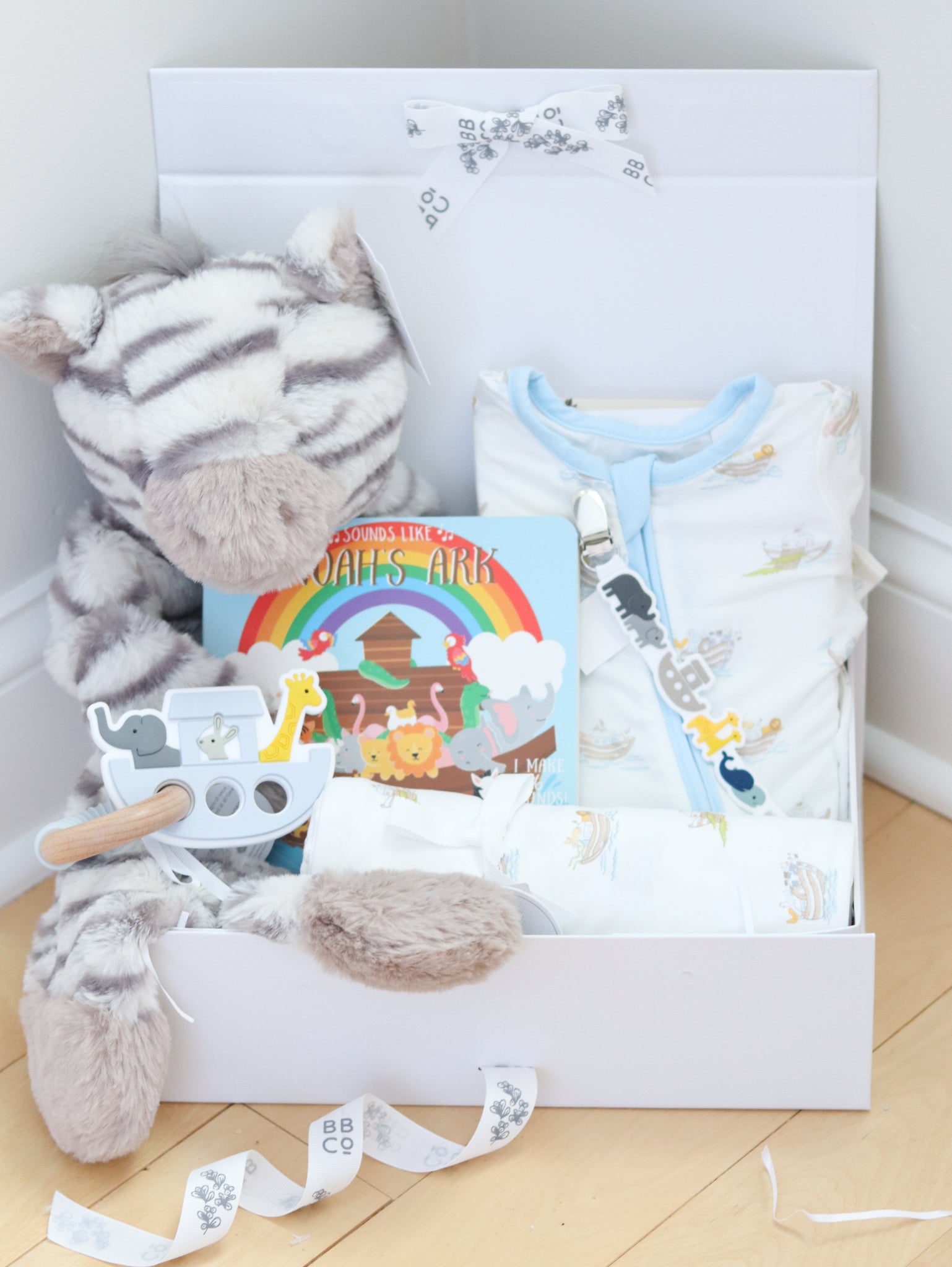 Gift box with plush toy, baby bib, and book on a wooden floor.