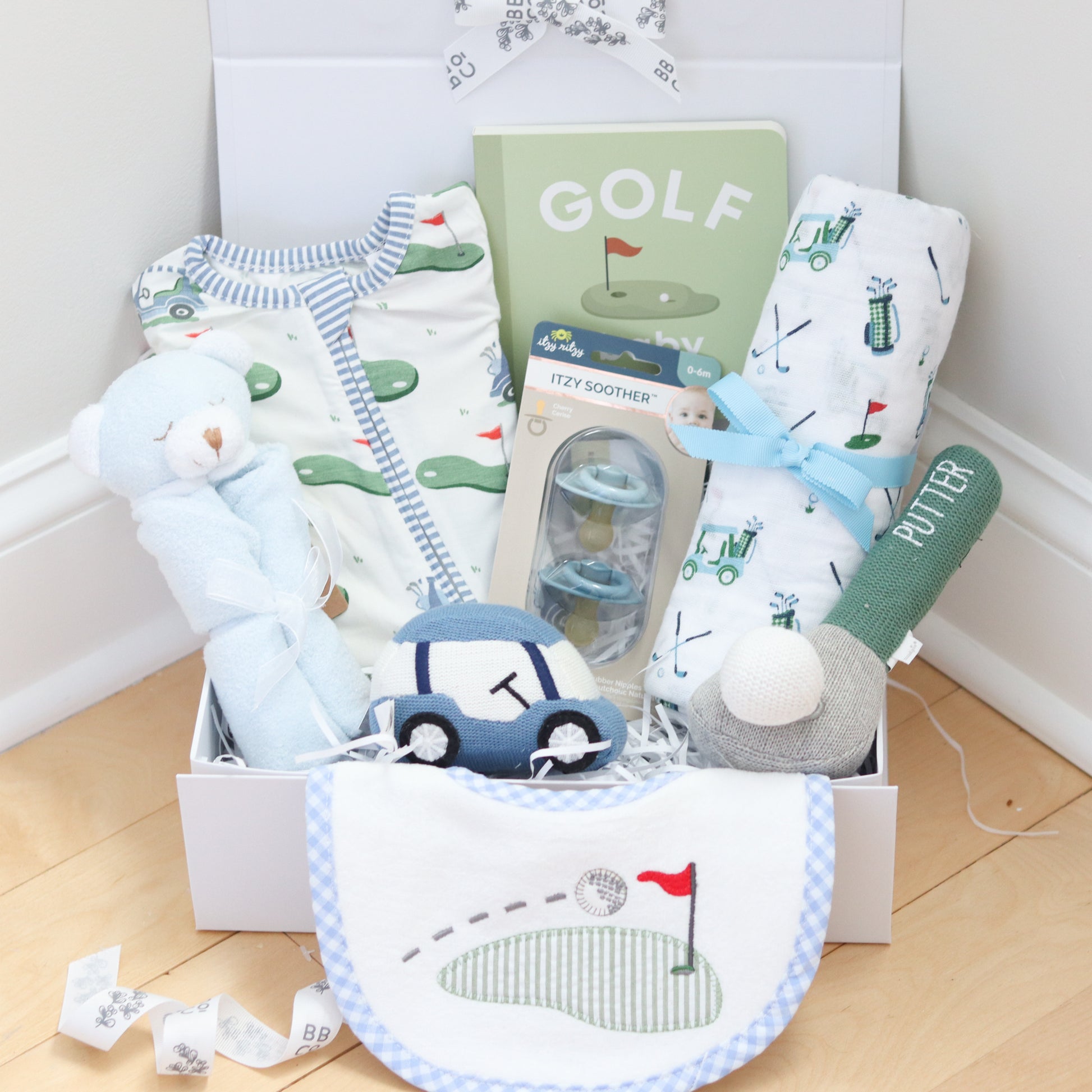 Golf Baby gift set with baby clothes, toys, and a book titled 'Golf' on a wooden floor.