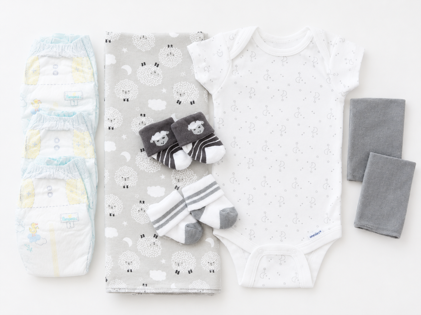 A baby clothing and diaper set arranged on a white background, including a white short-sleeve bodysuit with tiny gray motifs, a gray blanket with a white sheep print, a pair of dark gray and white striped socks with sheep faces, a pair of folded gray cloth diapers, and a pair of folded gray washcloths.