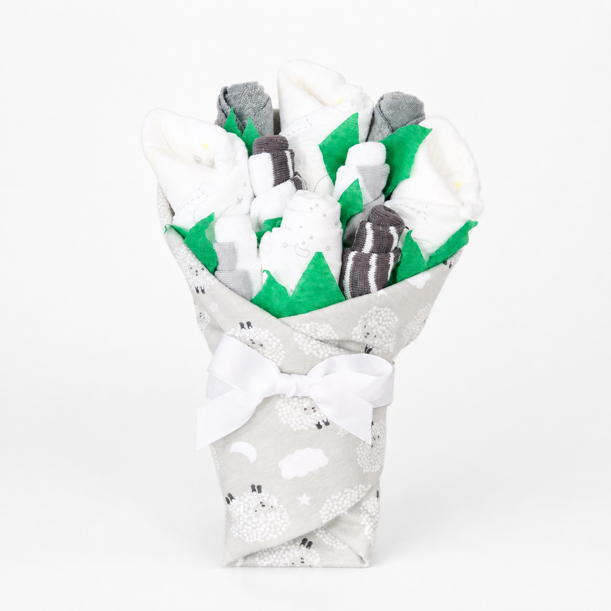 A baby shower gift set wrapped in a fabric bouquet sleeve with a white sheep print, tied with a white bow. Inside the wrapper, baby socks in white, gray, and black are arranged with green felt accents.